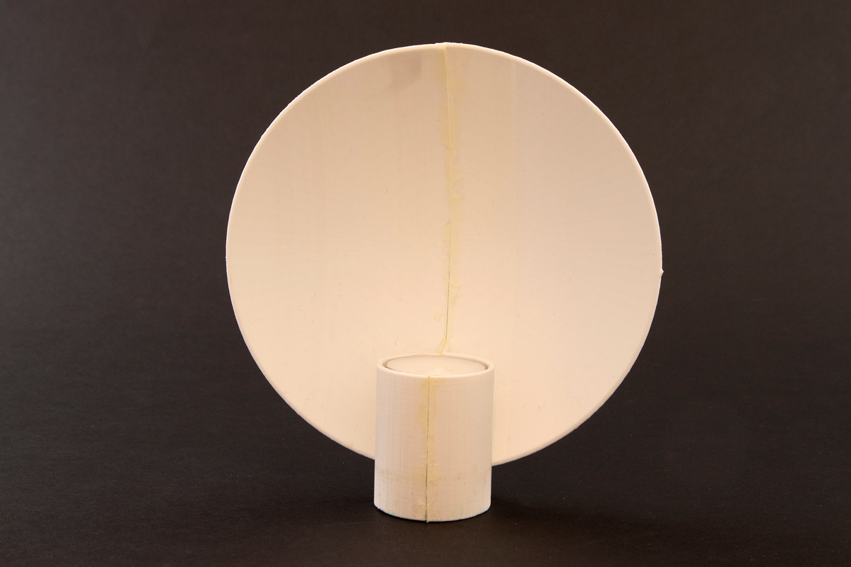 Vegglampe i messing. Rund parabolformet skive med telysholder foran. Rektangulært feste på baksiden med en avstandsplate mellom feste og parabol. Designet tar opp i seg den pre-elektriske lampetypen med reflektorskjerm. 

To 3D-printede protyper i plast. En hvit prototyp for en bordversjon av lampen, som har en rund parabol festet til en høy sylinder. Sylinderen fungerer som både fot og telysholder. Grønt kitt under basen.
 
Gul prototyp for vegglampen. Samme utforming som messinglampen, men har ikke rektangulært feste med avstandsplate på samme måten. Avstandsplaten på prototypen er festet på nedre halvdel av parabolen, og veggfestet er festet direkte på parabolen.