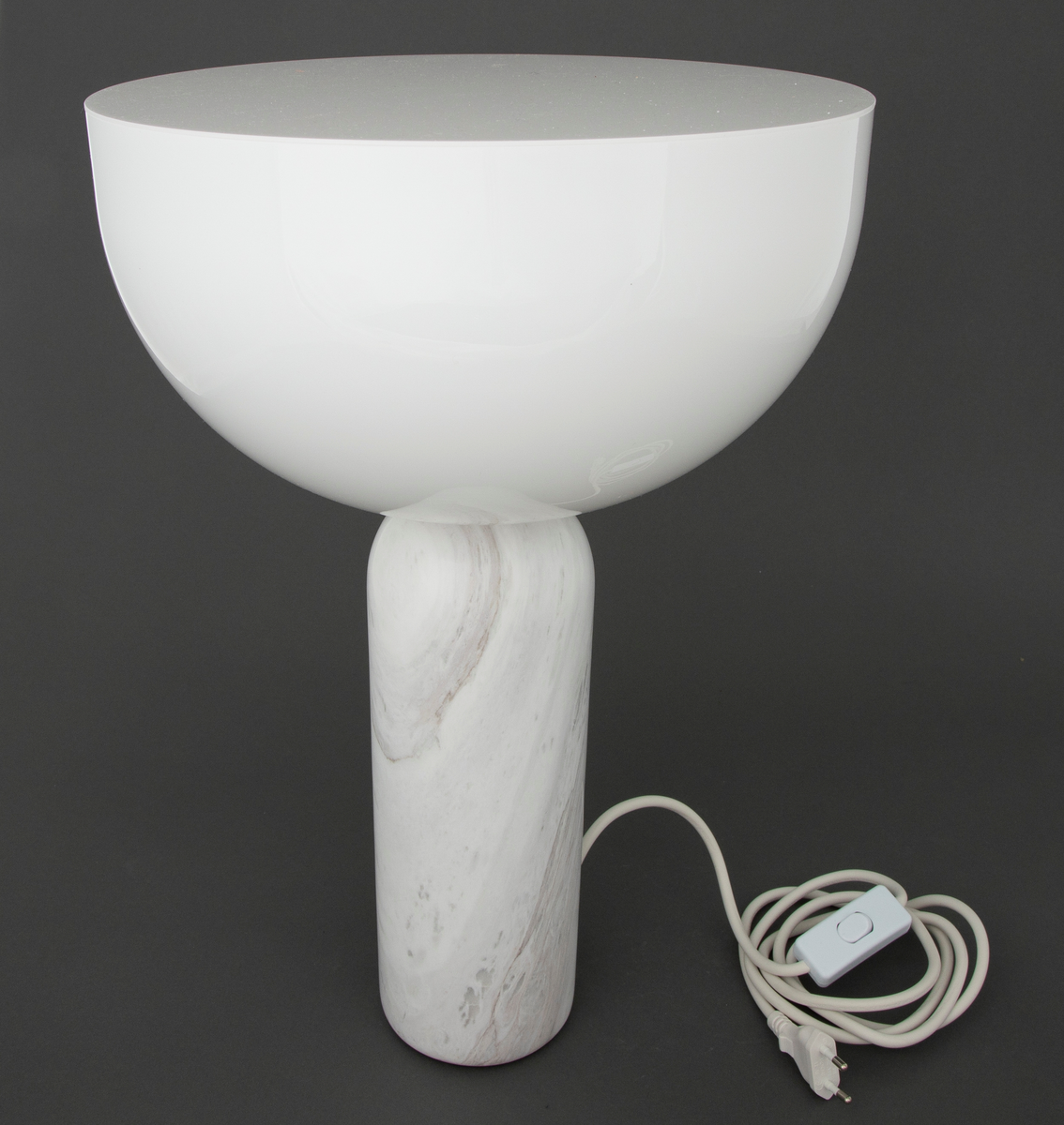 Lampe i dreiet marmor og injeksjonsstøpt akryl. Sylinderformet sokkel i marmor med mykt avrundet øvre del, som møter en halvkuleformet skjerm i akryl.