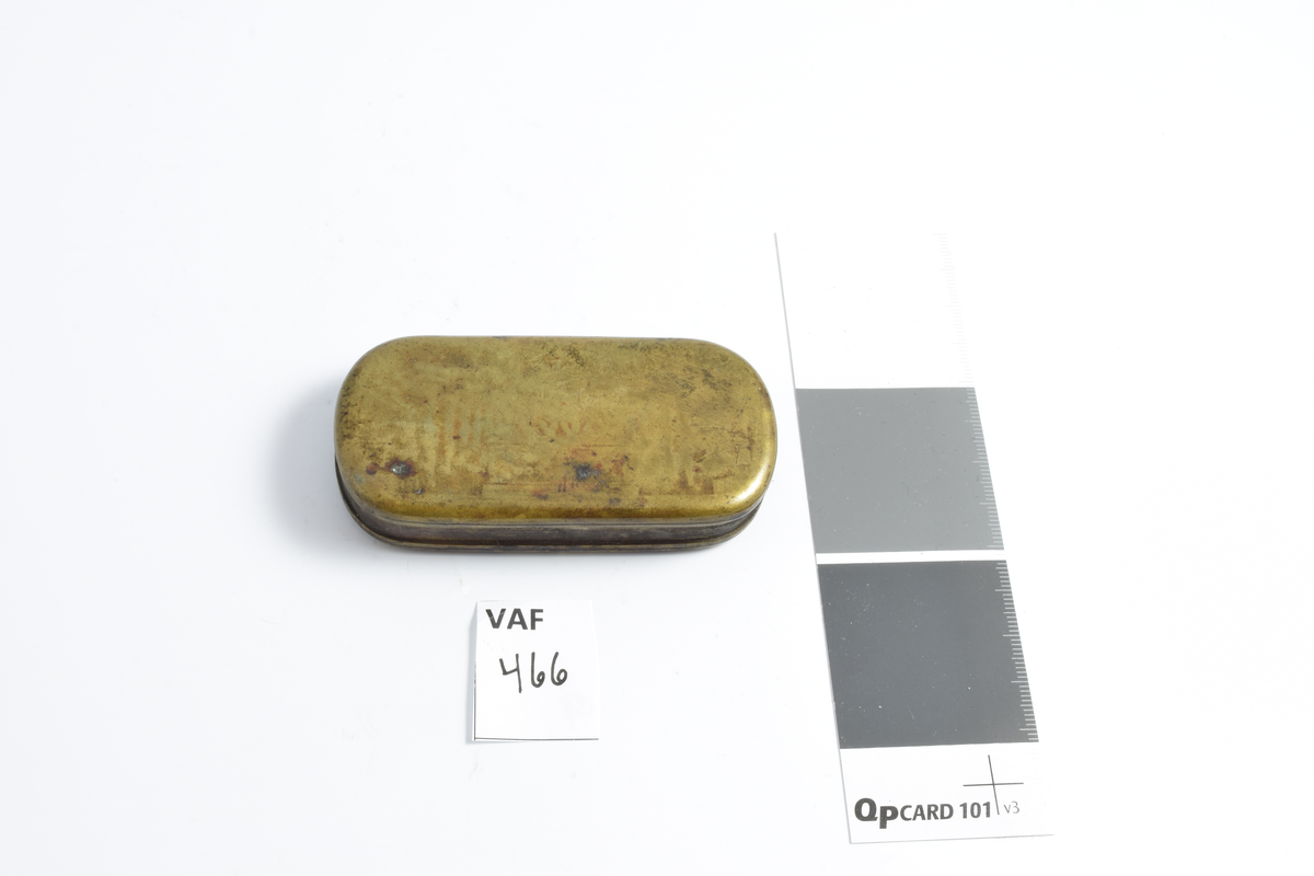 Snusdåse i messing. Firkantet med runde hjørner, flat bunn og lokk. Lokket viser spor av plastisk dekorasjon.