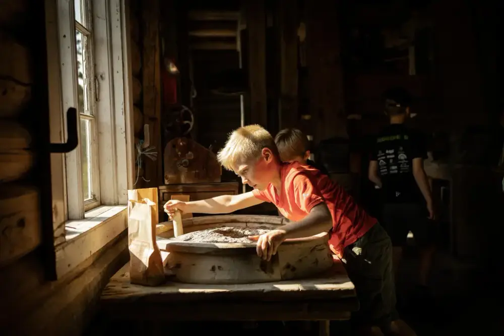 Barn prøver ut håndkverna på Eggedal Mølle, tungt arbeid for en liten kropp.