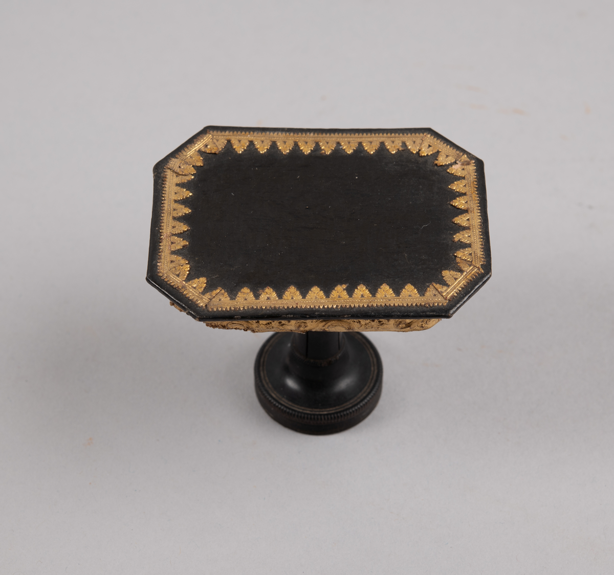 Bord til dukkehus. 8-kantet bordplate med gulldekor langs kanten. En dreid søylefot.