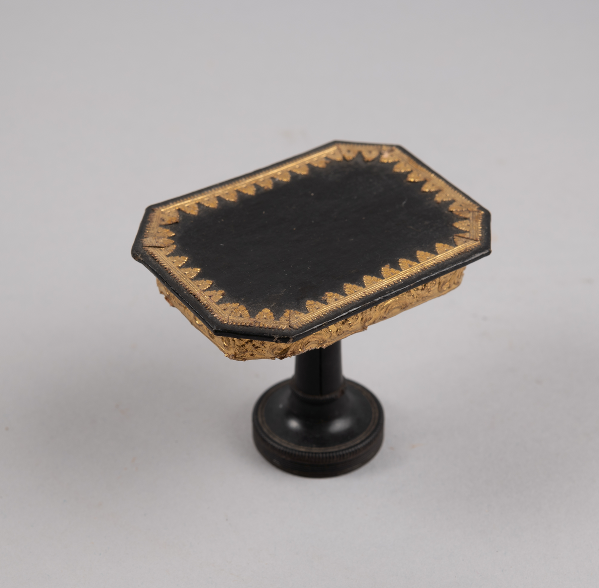 Bord til dukkehus. 8-kantet bordplate med gulldekor langs kanten. En dreid søylefot.