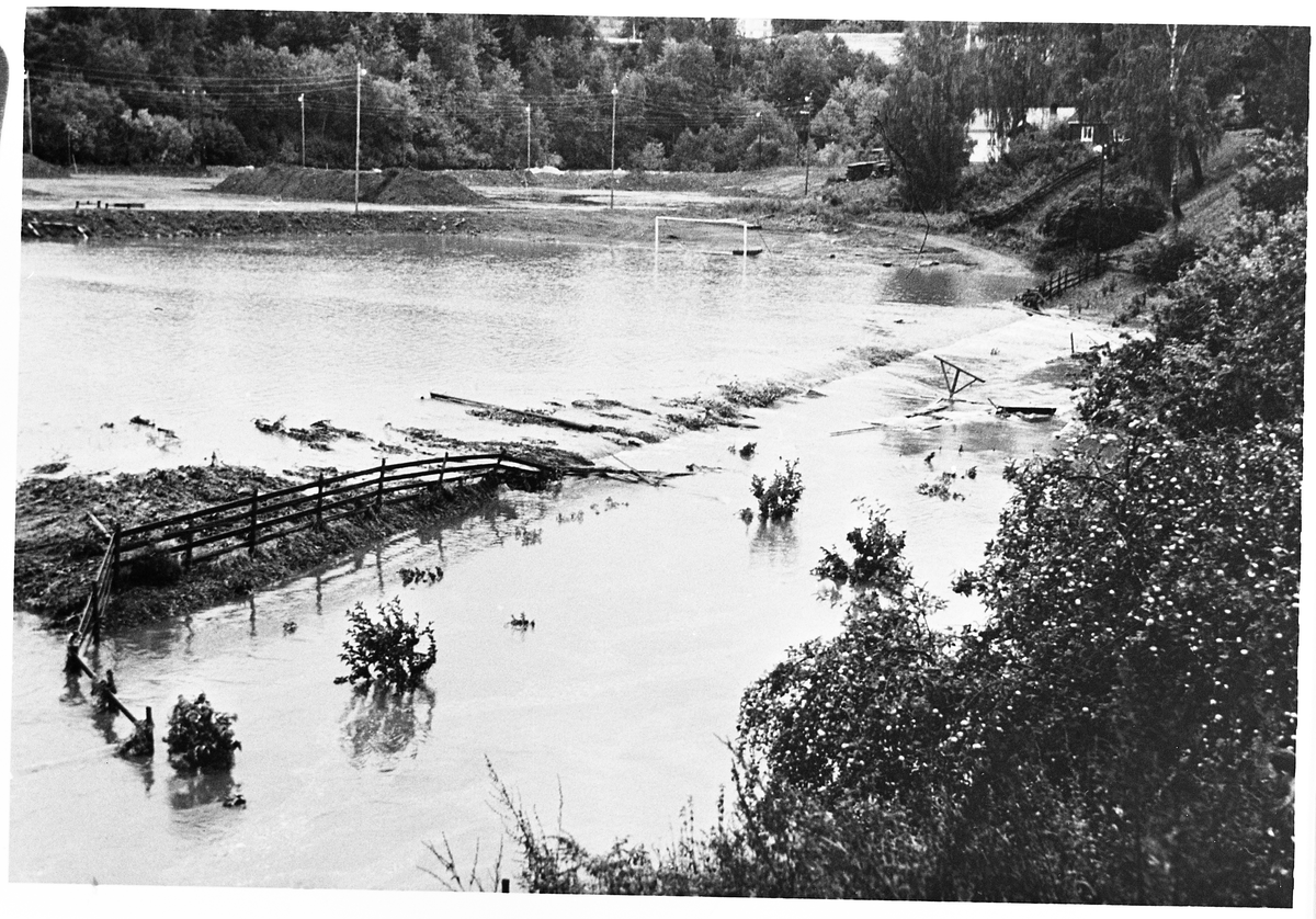 Flom i Slukelva og Lenaelva.
Etter kraftig regn 12. september 1956 gikk elva over sine bredder på flere steder.  I bakgrunnen til høyre ser vi badstua og vi ser vannet har tatt med seg skigarden mellom plassen og hagene til Skramstad og fotograf Berger.