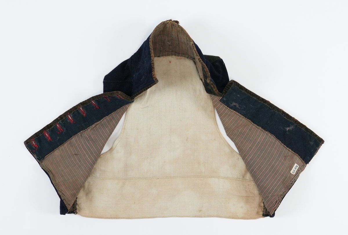 Vest sydd av mørkeblått klede med rygg av linlerret. Framstykka er fôra med stripet toskaft bomulssstoff i brunt, raudt og grått. På høgre framstykke åtte knapphol sydde med raud kameltråd, på venstre åtte runde metallknappar med pålodda hemper. Knappane er støypte skillingsknappar, nokre graverte. Slitne. Høg ståkrage stukken med prikkesting av ubleika lingarn. Krage og opning kanta med brune (svarte?) flyelsband. Fôr bak knapper av blått ribbet ullstoff.
