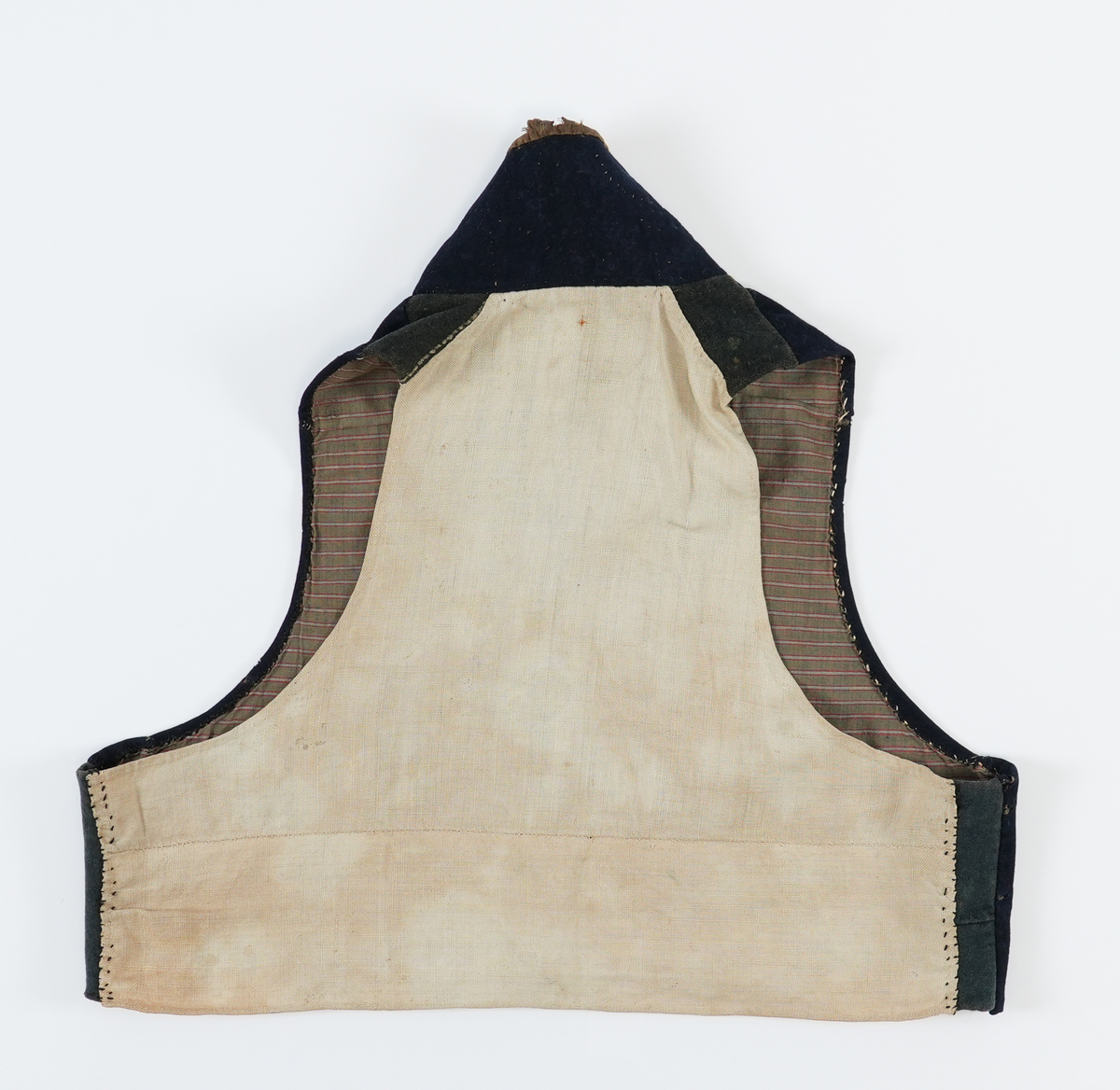 Vest sydd av mørkeblått klede med rygg av linlerret. Framstykka er fôra med stripet toskaft bomulssstoff i brunt, raudt og grått. På høgre framstykke åtte knapphol sydde med raud kameltråd, på venstre åtte runde metallknappar med pålodda hemper. Knappane er støypte skillingsknappar, nokre graverte. Slitne. Høg ståkrage stukken med prikkesting av ubleika lingarn. Krage og opning kanta med brune (svarte?) flyelsband. Fôr bak knapper av blått ribbet ullstoff.
