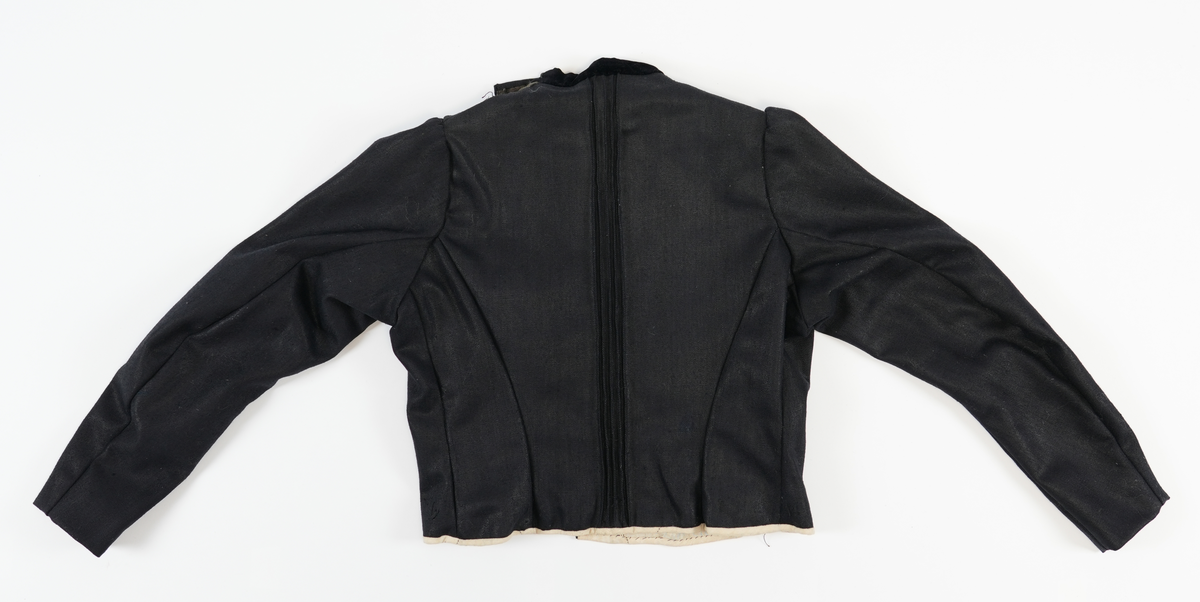 Svart jakke i ullstoff med kvitt linfôr. Dekorelement i form av biser (tre sett med fem bretter), fløyelstoff på kragen og fire falske knapper på framstykket. Svarte glassperlebånd er sydd som dekor rundt fronten på jakka og skjuler åpningen. To innsnitt på sidene av framstykket. Jakka festast saman av 17 hekter på høgre framstykket (påkledd) og fire på venstre skulder (påkledd). Opning midt framme som ein lukka med 12 metallhekter. For å skjule denne lukkinga bretta ein over dekorstykket. Nedre del av dekorstykket vert festa med fire metallhekter i venstre framstykket. Øvre del av dekorstykket vert festa med ei metallhekte, frå venstre til høgre. Nederste del av jakka har kvitt kanteband av lin. Jakka har puffermer. Bakstykket har fire biser midt på ryggen. Ryggen er satt saman av tre stoffsykker som forma jakka etter kroppsfasong. 

Innsida av halsopningen er kanta med eit grønnbrunt band av bomull (?). Heile jakka er sydd med maskin, men med noko hansaum på detaljane. Saumane på innsida ber preg av å ha blitt sydd ut slik at jakka vert større. 