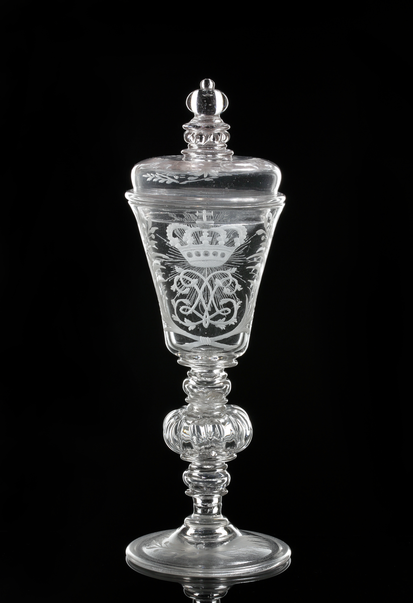 Vinglas med lock. Klockformad kupa och profilarat ben bestående av påklippta blåsta detaljer och batsar.
Graverad kunglig krona över drottning Lovisa Ulrikas monogram "LU". På motstående sida Nordstjärnan och på sidorna blomrankor. På locket och foten bladrankor.
Inskrivet i huvudkatalogen 1946.