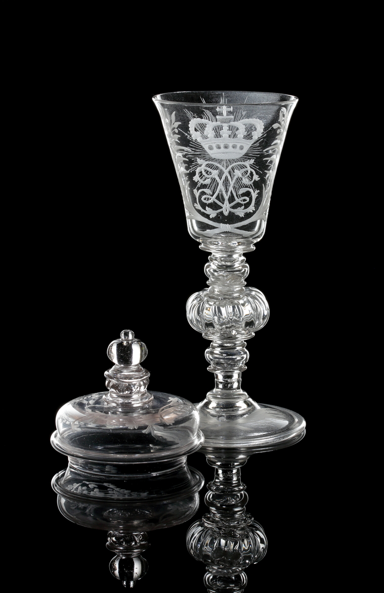 Vinglas med lock. Klockformad kupa och profilarat ben bestående av påklippta blåsta detaljer och batsar.
Graverad kunglig krona över drottning Lovisa Ulrikas monogram "LU". På motstående sida Nordstjärnan och på sidorna blomrankor. På locket och foten bladrankor.
Inskrivet i huvudkatalogen 1946.