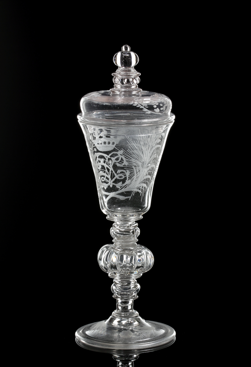 Vinglas med lock. Klockformad kupa och profilarat ben bestående av påklippta blåsta detaljer och batsar.
Graverad kunglig krona över drottning Lovisa Ulrikas monogram "LU". På motstående sida Nordstjärnan och på sidorna blomrankor. På locket och foten bladrankor.
Inskrivet i huvudkatalogen 1946.