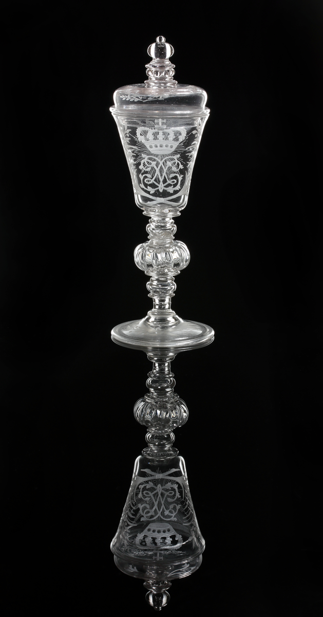 Vinglas med lock. Klockformad kupa och profilarat ben bestående av påklippta blåsta detaljer och batsar.
Graverad kunglig krona över drottning Lovisa Ulrikas monogram "LU". På motstående sida Nordstjärnan och på sidorna blomrankor. På locket och foten bladrankor.
Inskrivet i huvudkatalogen 1946.