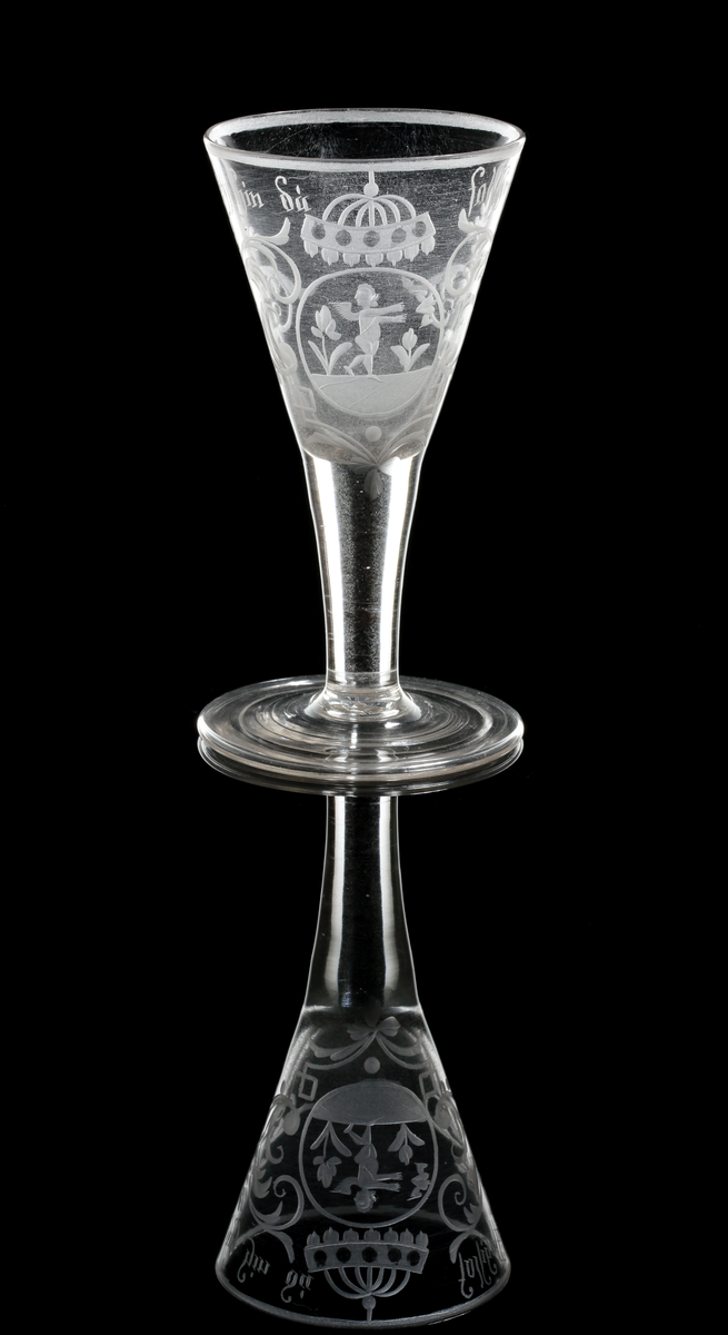 Vinglas av spetsglasmodell med konisk kupa som övergår i ett draget ben, Graverat motiv i form av en medaljon gm ed en amorin som sträcker sig efter ett bevingat hjärta, och över detta något som troligen är en krona. Motivet flankeras av växtmotiv, samt texten "Geh hin.... du falseher sin" som är placerad under mynningen.
Inskrivet i huvudkatalogen 1964.