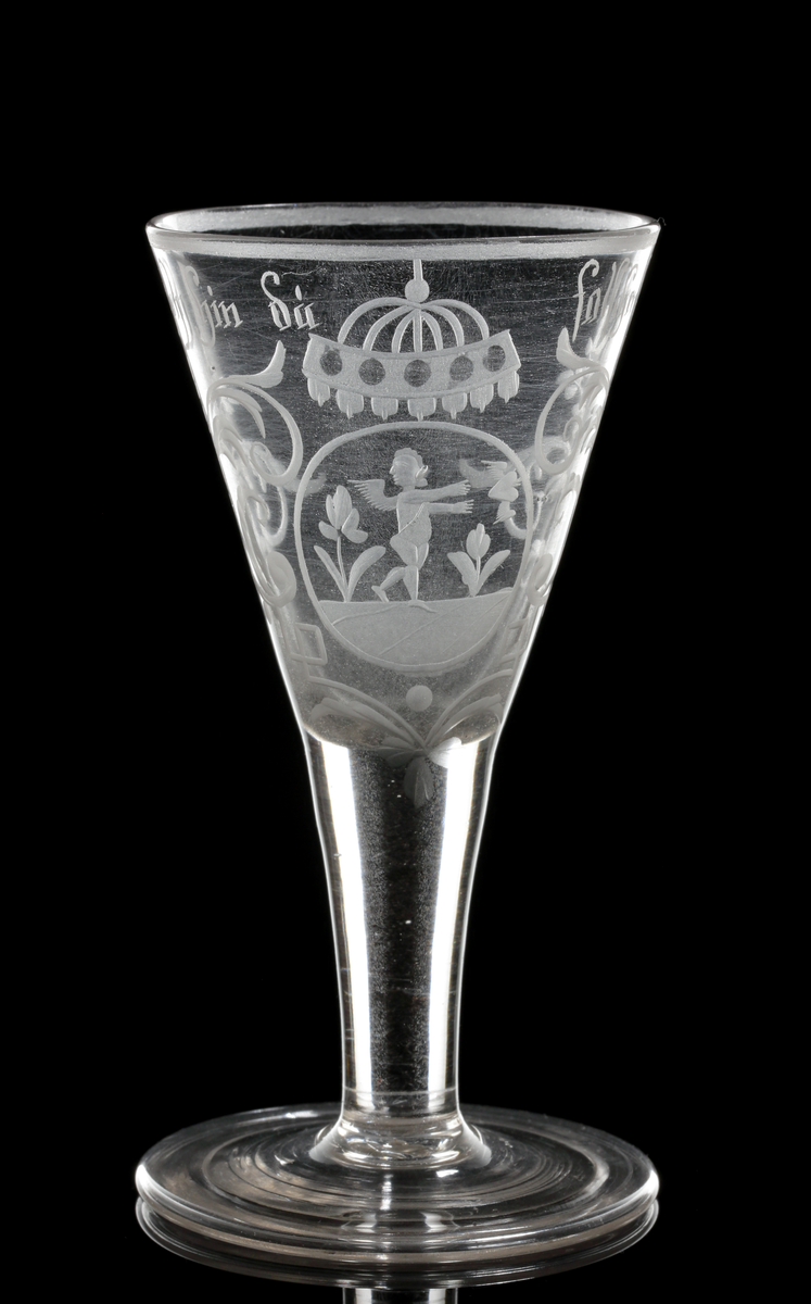 Vinglas av spetsglasmodell med konisk kupa som övergår i ett draget ben, Graverat motiv i form av en medaljon gm ed en amorin som sträcker sig efter ett bevingat hjärta, och över detta något som troligen är en krona. Motivet flankeras av växtmotiv, samt texten "Geh hin.... du falseher sin" som är placerad under mynningen.
Inskrivet i huvudkatalogen 1964.