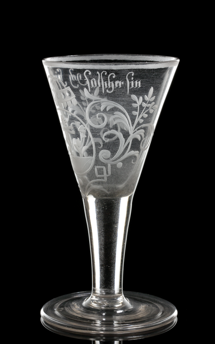 Vinglas av spetsglasmodell med konisk kupa som övergår i ett draget ben, Graverat motiv i form av en medaljon gm ed en amorin som sträcker sig efter ett bevingat hjärta, och över detta något som troligen är en krona. Motivet flankeras av växtmotiv, samt texten "Geh hin.... du falseher sin" som är placerad under mynningen.
Inskrivet i huvudkatalogen 1964.