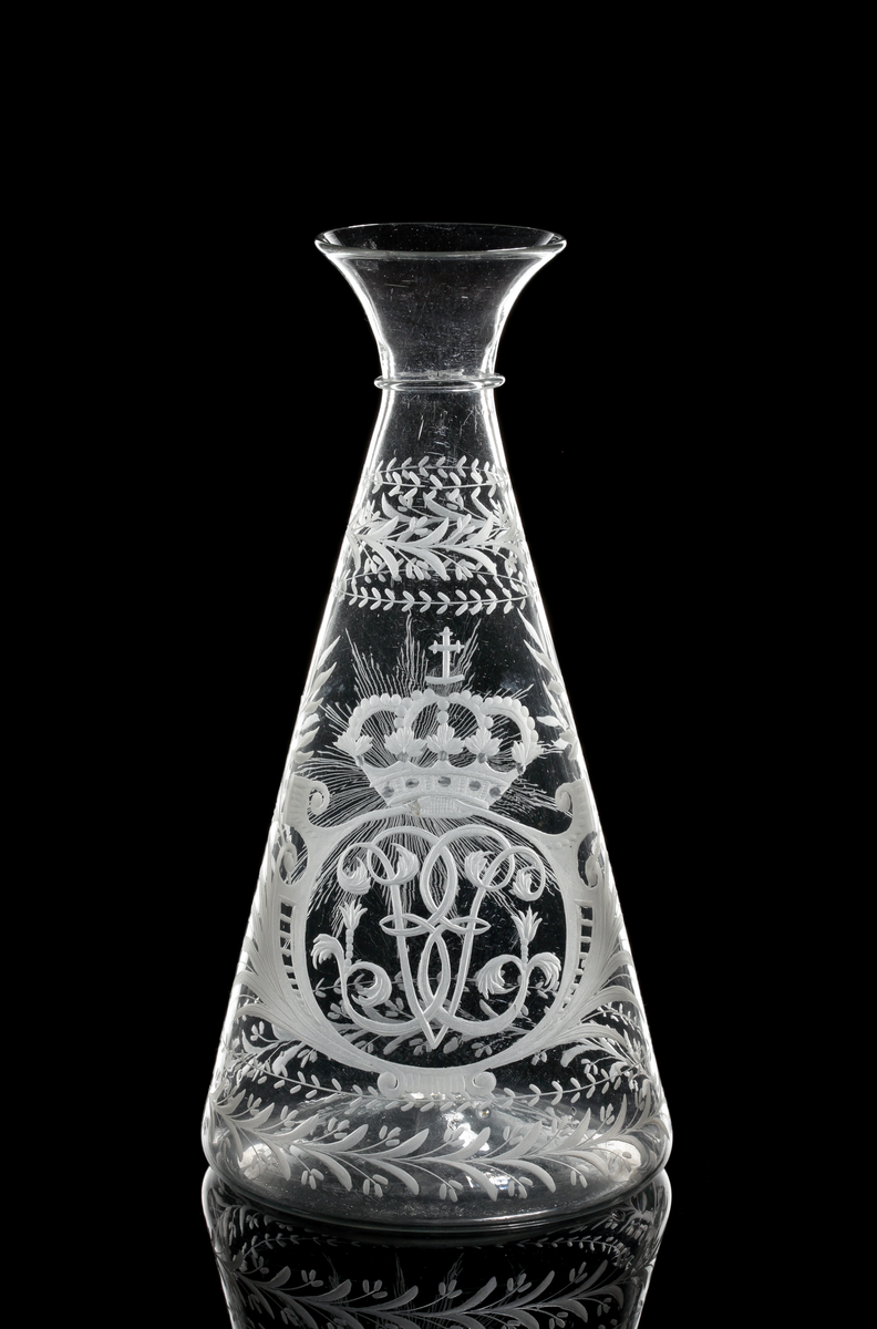Vinkaraff av konisk modell med påklippt tråd under den vidgande mynningen. Graverad med drottning Ulrika Eleonoras monogram under kunglig krona, flankerad av kvistar av palm- och lagerblad. Växtmotiv runt skuldra och botten. På motsatt sidan en strålande nordstjärna.
Inskriven i huvudkatalogen 1970.