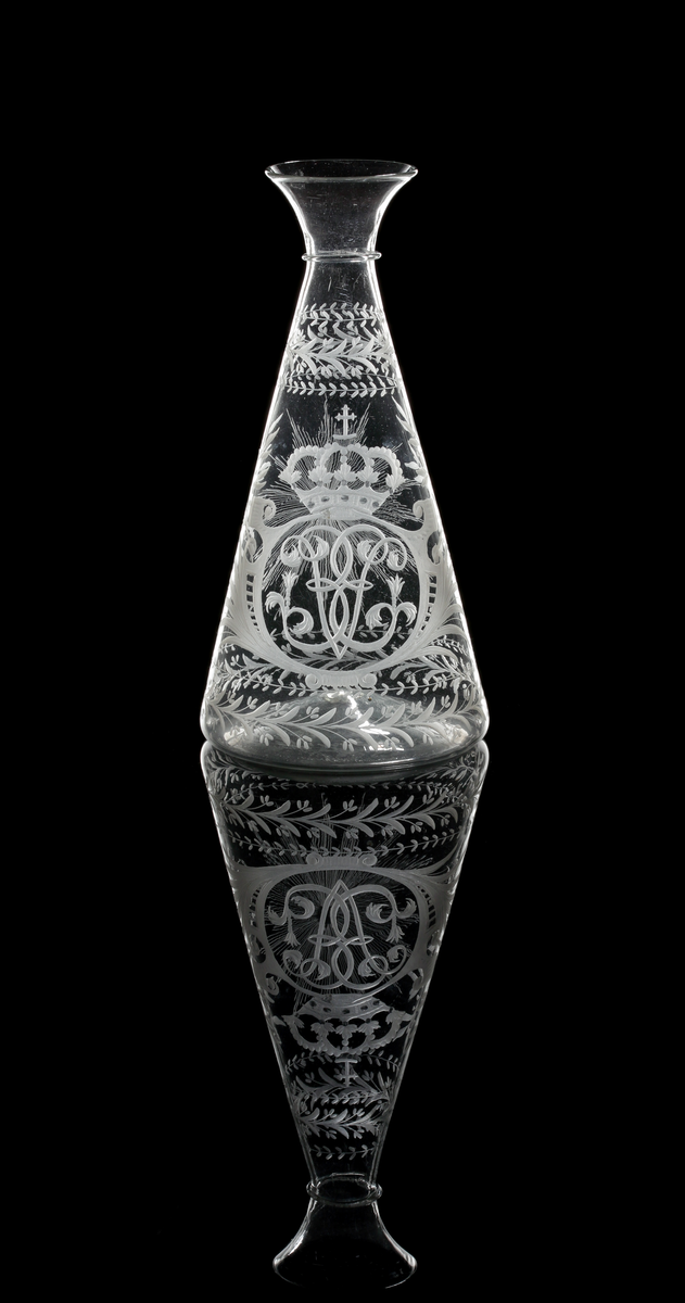 Vinkaraff av konisk modell med påklippt tråd under den vidgande mynningen. Graverad med drottning Ulrika Eleonoras monogram under kunglig krona, flankerad av kvistar av palm- och lagerblad. Växtmotiv runt skuldra och botten. På motsatt sidan en strålande nordstjärna.
Inskriven i huvudkatalogen 1970.