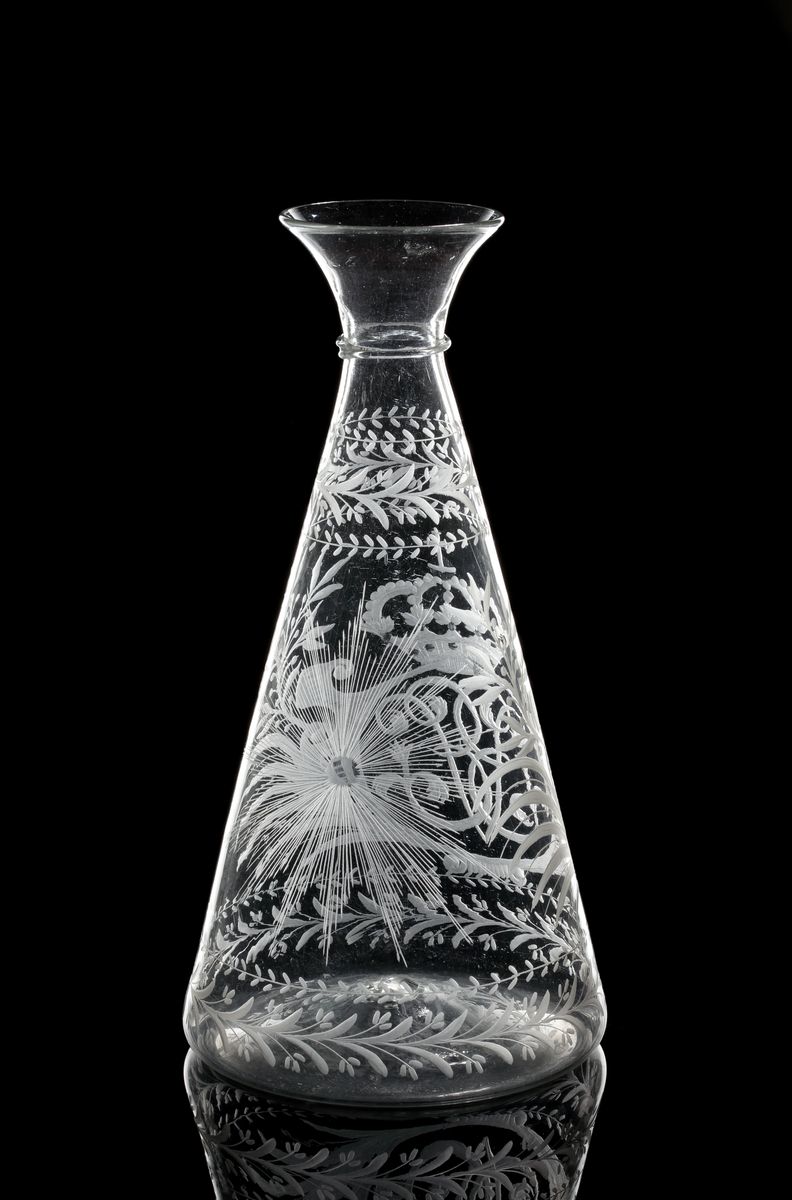 Vinkaraff av konisk modell med påklippt tråd under den vidgande mynningen. Graverad med drottning Ulrika Eleonoras monogram under kunglig krona, flankerad av kvistar av palm- och lagerblad. Växtmotiv runt skuldra och botten. På motsatt sidan en strålande nordstjärna.
Inskriven i huvudkatalogen 1970.