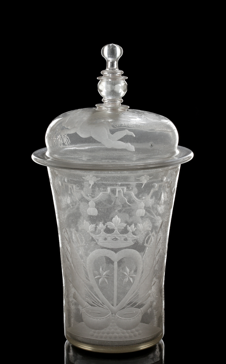 Bägare med lock. Svagt vidgande mot mynningen. Lock med profilared knopp som facettslipats.
Gravyr: Alliansvapen; syftar på greve Nils Gyllenstierna af Fogelvik (1648-1720) förmäld 1680 med Anna Christina Gyllenstierna af Björksund och Helgö (1657-1715). Bacchus dragen av två getter. På locket putti och text: "Le vien nous Menne a la gloire Bachus nous donne la victoire."
Inskrivet i huvudkatalogen 1936.