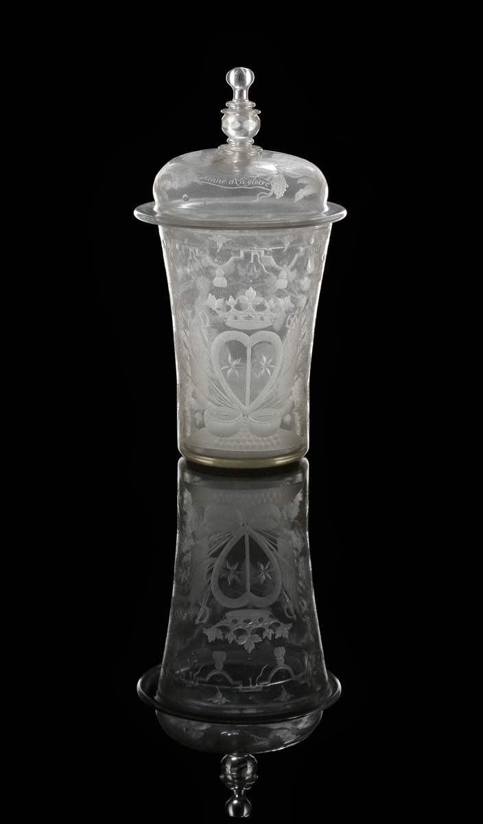 Bägare med lock. Svagt vidgande mot mynningen. Lock med profilared knopp som facettslipats.
Gravyr: Alliansvapen; syftar på greve Nils Gyllenstierna af Fogelvik (1648-1720) förmäld 1680 med Anna Christina Gyllenstierna af Björksund och Helgö (1657-1715). Bacchus dragen av två getter. På locket putti och text: "Le vien nous Menne a la gloire Bachus nous donne la victoire."
Inskrivet i huvudkatalogen 1936.