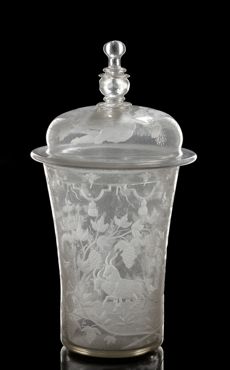 Bägare med lock. Svagt vidgande mot mynningen. Lock med profilared knopp som facettslipats.
Gravyr: Alliansvapen; syftar på greve Nils Gyllenstierna af Fogelvik (1648-1720) förmäld 1680 med Anna Christina Gyllenstierna af Björksund och Helgö (1657-1715). Bacchus dragen av två getter. På locket putti och text: "Le vien nous Menne a la gloire Bachus nous donne la victoire."
Inskrivet i huvudkatalogen 1936.