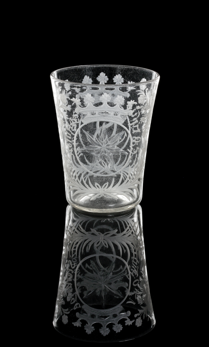 Bägare tillhör "Steningeservisen". 
Cylindrisk, vidgad uppåt. Graverad dekor: Blommönster. På ena sidan Gyllenstiernas monogram under grevlig krona med text runt om: "Häj luftig haisa vivat". På andra sidan: Gyllenstiernas vapen (sjustrålig stjärna) med text runt om: "Steninge 1705".
Följande text finns skriven i huvudkatalogen för M 9768 och vinglas M 9769:
Beskrivet av docent Heribert Seitz i brev till arkitekt P. Boberg av den 19 okt. 1937: "De härstammar från Gyllenstiernska godset Steninge (i Upland), ha alltid gått i arv och tillhört en Fru Bib Adelsköld. De äro fullkomligt unika. Den ofrånkomliga glassjukan har jag behandlat. Det gäller i främsta hand tre föremål."
Bägaren påminner närmast om figur 8:2, sid. 71, jfr plansch 25 C i min avhandling". (Seitz ?)
Inskrivet i huvudkatalogen 1937.