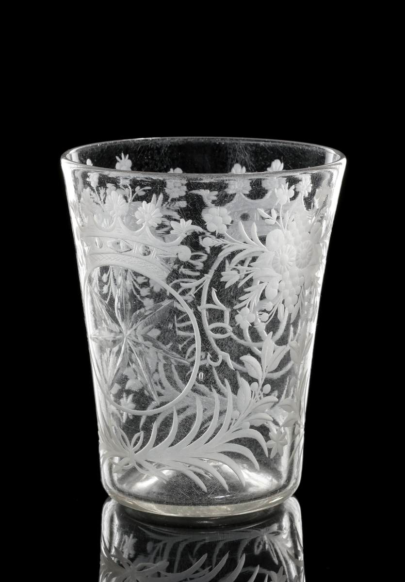 Bägare tillhör "Steningeservisen". 
Cylindrisk, vidgad uppåt. Graverad dekor: Blommönster. På ena sidan Gyllenstiernas monogram under grevlig krona med text runt om: "Häj luftig haisa vivat". På andra sidan: Gyllenstiernas vapen (sjustrålig stjärna) med text runt om: "Steninge 1705".
Följande text finns skriven i huvudkatalogen för M 9768 och vinglas M 9769:
Beskrivet av docent Heribert Seitz i brev till arkitekt P. Boberg av den 19 okt. 1937: "De härstammar från Gyllenstiernska godset Steninge (i Upland), ha alltid gått i arv och tillhört en Fru Bib Adelsköld. De äro fullkomligt unika. Den ofrånkomliga glassjukan har jag behandlat. Det gäller i främsta hand tre föremål."
Bägaren påminner närmast om figur 8:2, sid. 71, jfr plansch 25 C i min avhandling". (Seitz ?)
Inskrivet i huvudkatalogen 1937.