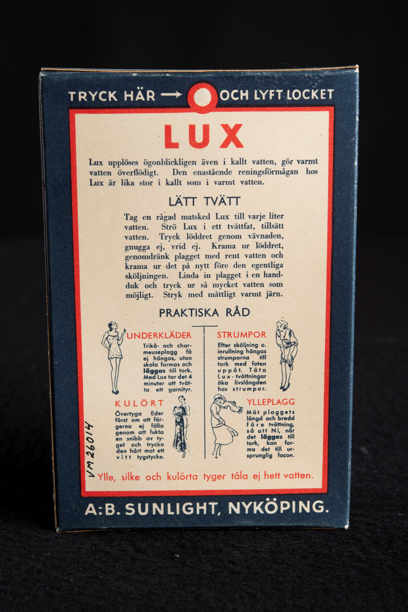 Förpackning av papp i mörkblå färg med text i vitt och rött. Formen är rektangulär, stående på höjden. Har innehållit tvålflingor, LUX Tvålflingor.