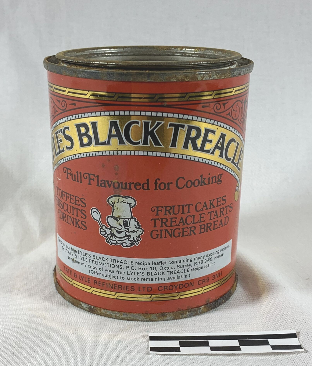 Metallboks med Lyle's Black Treacle, et britisk produkt brukt i tradisjonell matlaging. Boksen har en kapasitet på 1 lb (454 g) og er dekorert med røde, gule og svarte farger, med et ikonisk bilde av en kvinne som holder en kake, under slagordet "For Traditional Cooking." Boksen er sylinderformet og har et lokk som sannsynligvis har vært brukt til å forsegle det søte og mørke sirupsproduktet, kjent som treacle, som ofte brukes i baking.
