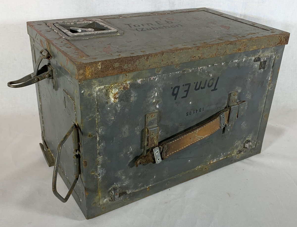Boks til oppbevaring av tilbehør til en tysk radiomottaker, merket "Torn. E. b" (Tornister Empfänger b), en bærbar radio brukt av det tyske militæret under andre verdenskrig. Esken er merket med serienummeret "134103" og har rester av originalmaling, som viser slitasje og rust på flere områder. Det er et bærehåndtak av lær på siden, samt en låsemekanisme for å sikre innholdet. Lokket har en liten ventil, merket med "Auf" og "Zu" (åpen/lukket).