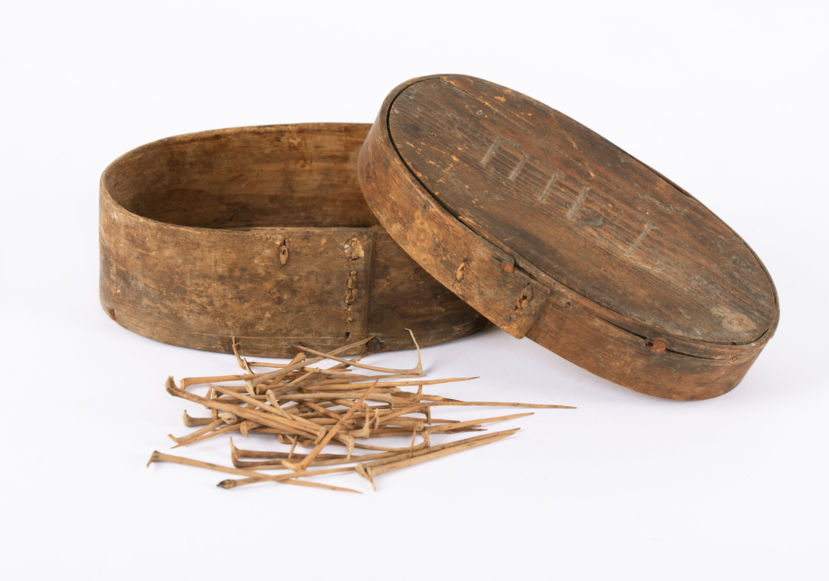 Sveipeeske med lokk, inneholder torner. Lokk og bunn festet til topp og bunn-plate med spiker. Esken er svakt trykk-dekorert med enkelt mønster, og inneholder pølsehorn og torner. Merket på innsiden.