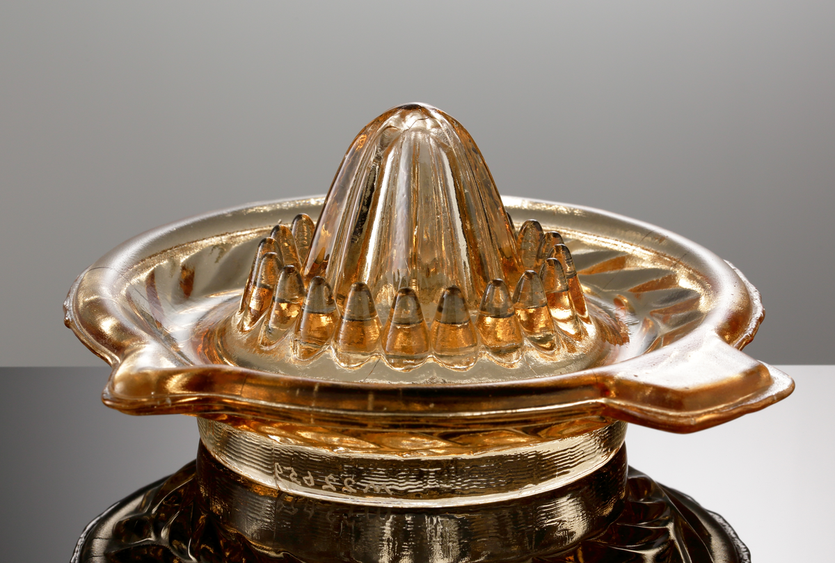 Citronpress.
Tillverkad på Sölvesborgs glasbruk (I=1896-1898, II=1914-1970).
Bladranka i relief på undersidan av brättet. Ojämn kant.
Svagt orangebrunt klarglas.

Inskrivet i huvudkatalogen 1974.