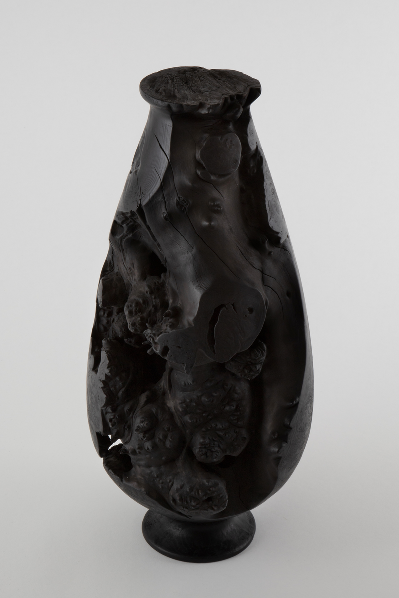 Vaseformet skulptur lagd av knoll fra hestekastanje. Høy og avlang form. Svartbrent med oljevoks.