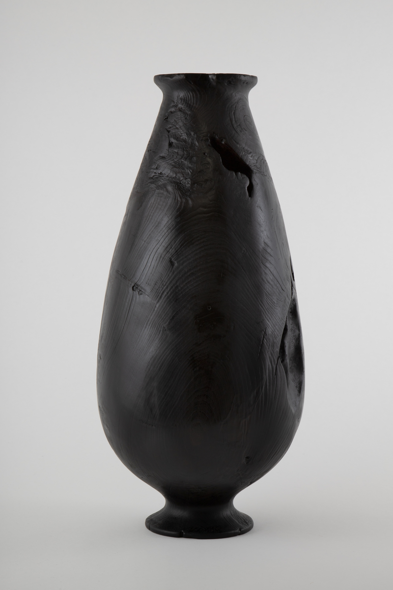 Vaseformet skulptur lagd av knoll fra hestekastanje. Høy og avlang form. Svartbrent med oljevoks.