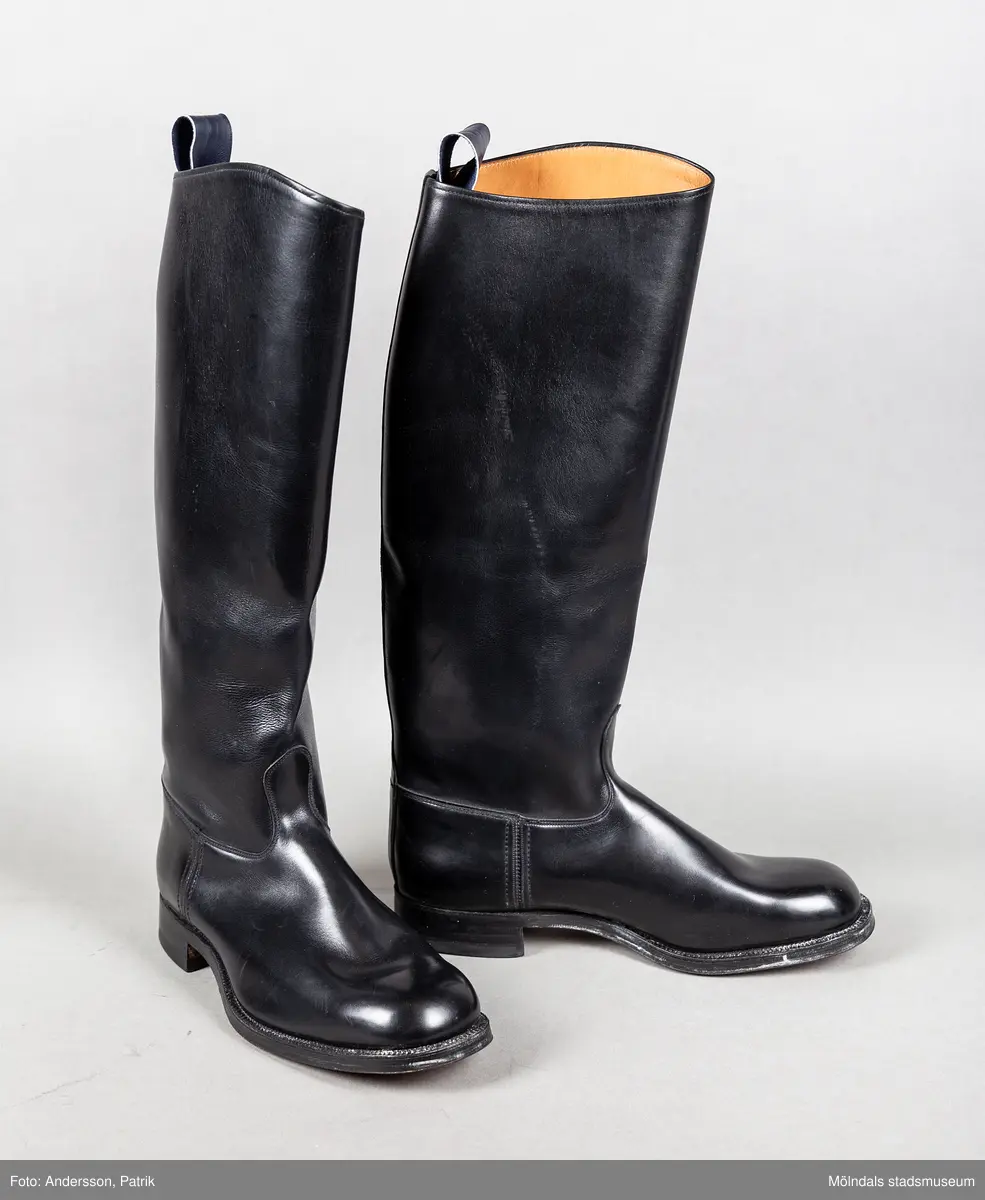 Ett par svarta ridstövlar i läder. Stövlarna är tillverkade på Ströms skofabrik i Kumla på 1950-talet och är mycket välgjorda. Dubbla sulor och handsydd randsula. Stövlarna har en flärp vid skaftets högsta punkt för att underlätta påklädning.  

Stövlarna hör till ridbyxor och härstammar från tidigt 50-tal.
Stövlarna tillhörde en flykting från Estland. Han flydde från Estland år 1944, under andra världskriget och var då 14 år gammal.
Stövlarna var tänkta att användas vid flykt, eftersom den tanken alltid fanns i bakhuvudet. Därför ville man vara väl förberedd med en för flykt passande klädsel.
Kläderna kom aldrig till användning för det de var avsedda till.