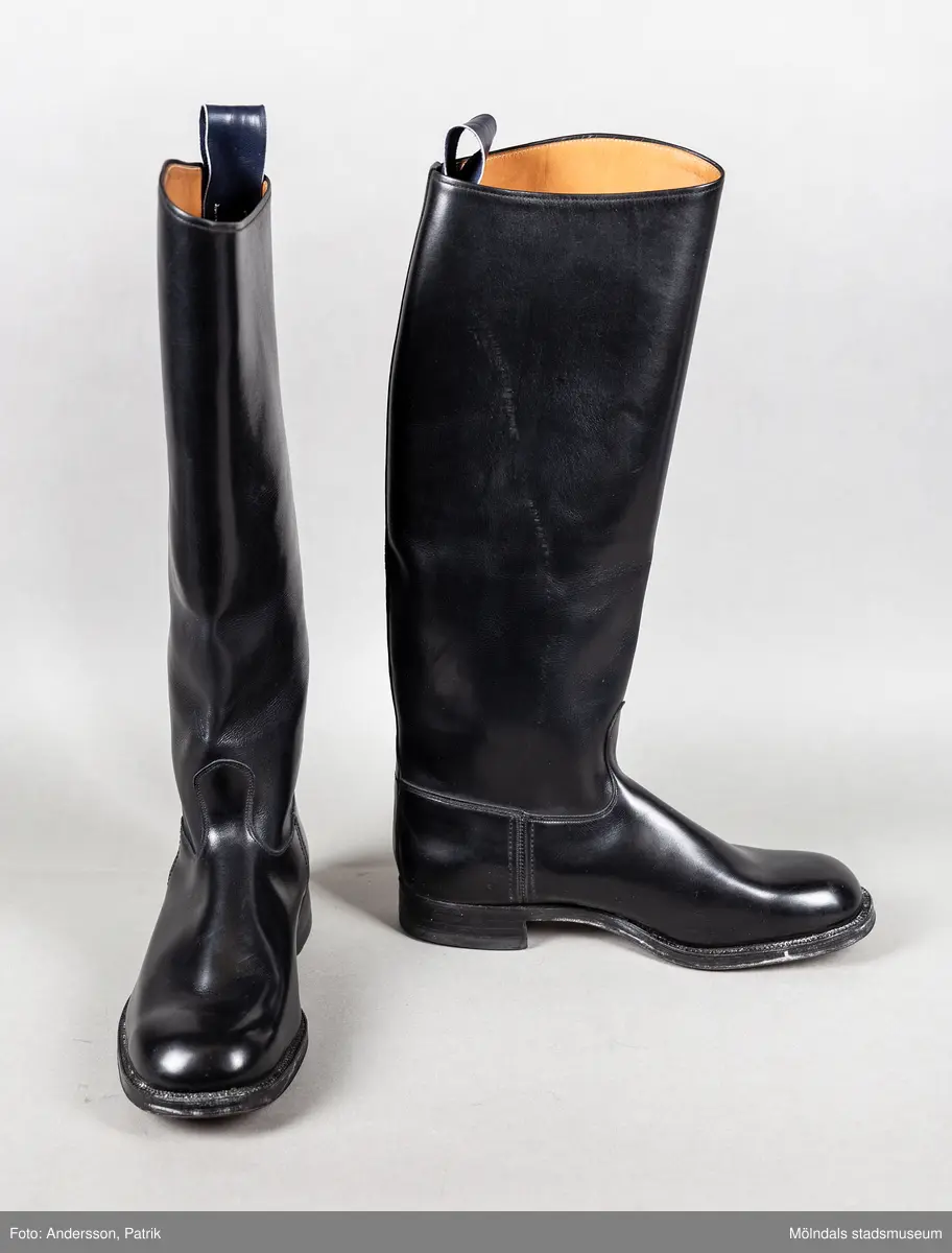 Ett par svarta ridstövlar i läder. Stövlarna är tillverkade på Ströms skofabrik i Kumla på 1950-talet och är mycket välgjorda. Dubbla sulor och handsydd randsula. Stövlarna har en flärp vid skaftets högsta punkt för att underlätta påklädning.  

Stövlarna hör till ridbyxor och härstammar från tidigt 50-tal.
Stövlarna tillhörde en flykting från Estland. Han flydde från Estland år 1944, under andra världskriget och var då 14 år gammal.
Stövlarna var tänkta att användas vid flykt, eftersom den tanken alltid fanns i bakhuvudet. Därför ville man vara väl förberedd med en för flykt passande klädsel.
Kläderna kom aldrig till användning för det de var avsedda till.