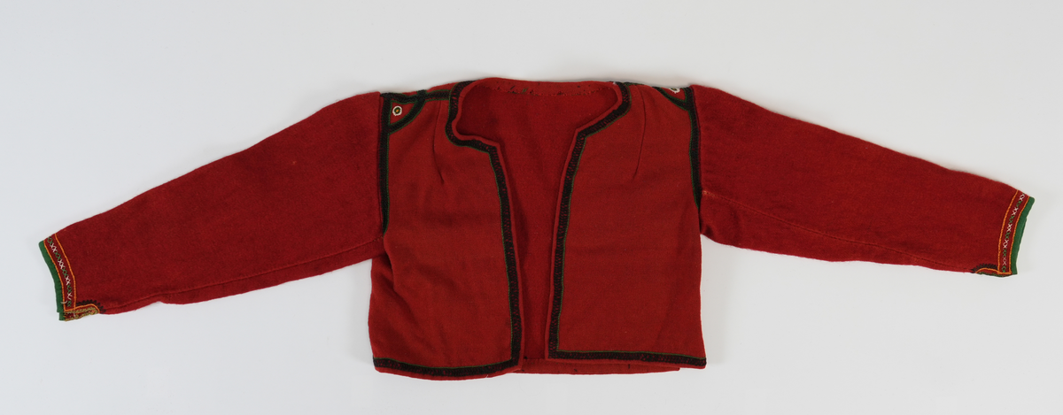 Trøye i tradisjonelt snitt. Open framme, hekta saman nede med krok og malje. Brodert rundt hals, framkant og nedrekant med doble kjedesting og kjedesting. På skuldra halvsirklar og med sirklar av knappholsting. Framme på era grøn kvarde, to rader med kjedesting og ei rad med to grøne og to kvite korssting vekslande.
Erma er gjenbruk frå ei gammal trøye