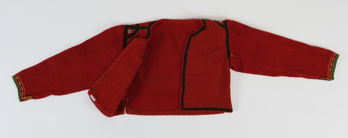 Trøye i tradisjonelt snitt. Open framme, hekta saman nede med krok og malje. Brodert rundt hals, framkant og nedrekant med doble kjedesting og kjedesting. På skuldra halvsirklar og med sirklar av knappholsting. Framme på era grøn kvarde, to rader med kjedesting og ei rad med to grøne og to kvite korssting vekslande.
Erma er gjenbruk frå ei gammal trøye