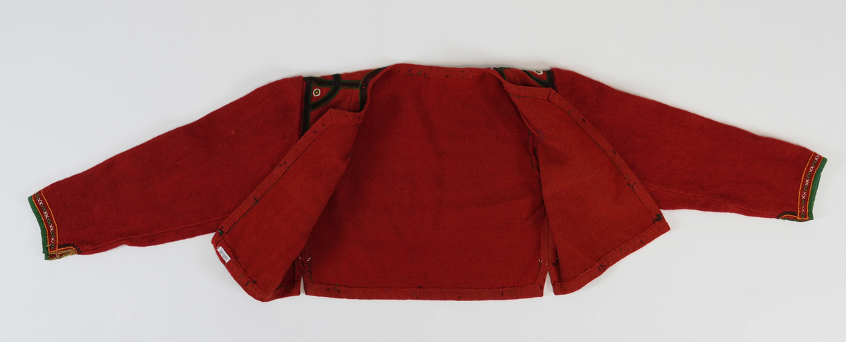 Trøye i tradisjonelt snitt. Open framme, hekta saman nede med krok og malje. Brodert rundt hals, framkant og nedrekant med doble kjedesting og kjedesting. På skuldra halvsirklar og med sirklar av knappholsting. Framme på era grøn kvarde, to rader med kjedesting og ei rad med to grøne og to kvite korssting vekslande.
Erma er gjenbruk frå ei gammal trøye