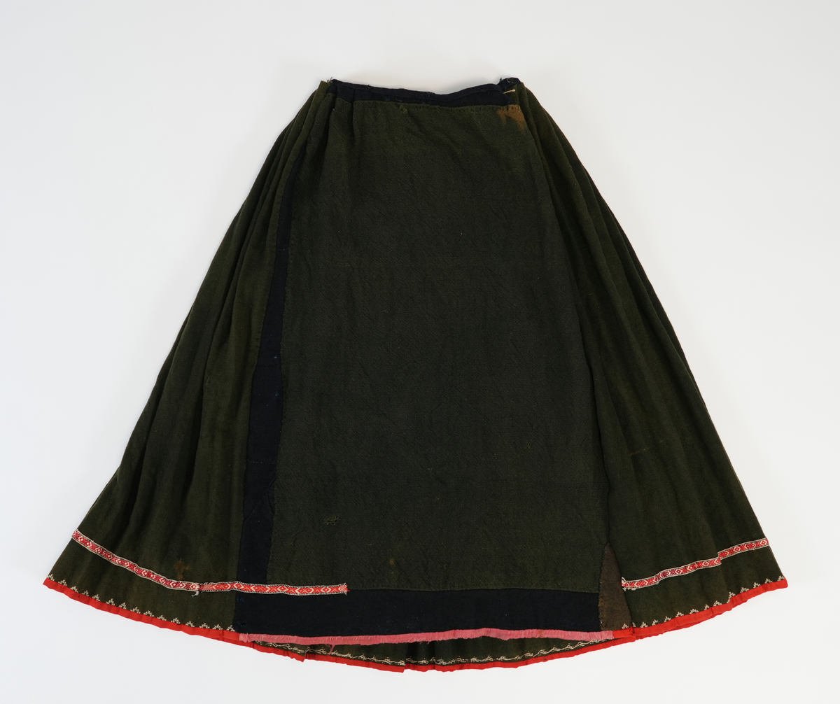 Stakk av grønn vadmel med grindvevd band og broderi langs skjørtekanten. Fangbredda er glatt med to folder i kvar side. Sydd av toskaft, påsett biter i blå krypertvevd vadmel. 

Stakken er sydd av fire høgder krypertvevd vadmel, fangbredden kjem i tillegg. 

Motfold midt bak, som i venstre "foldebunn". 19 folder på vestre og høgre side av motfolden. Avstand mellom foldletopen er 4.5-6 cm. 

