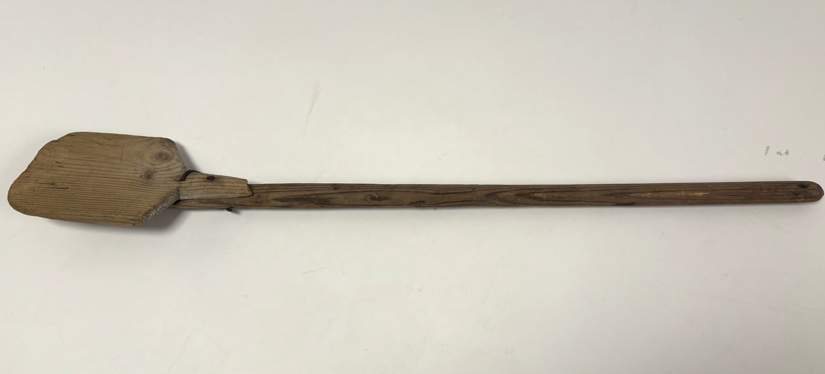 Handlaga spade i tre. Eit langt skaft og eit spadeblad som er spikra fast til skaftet.