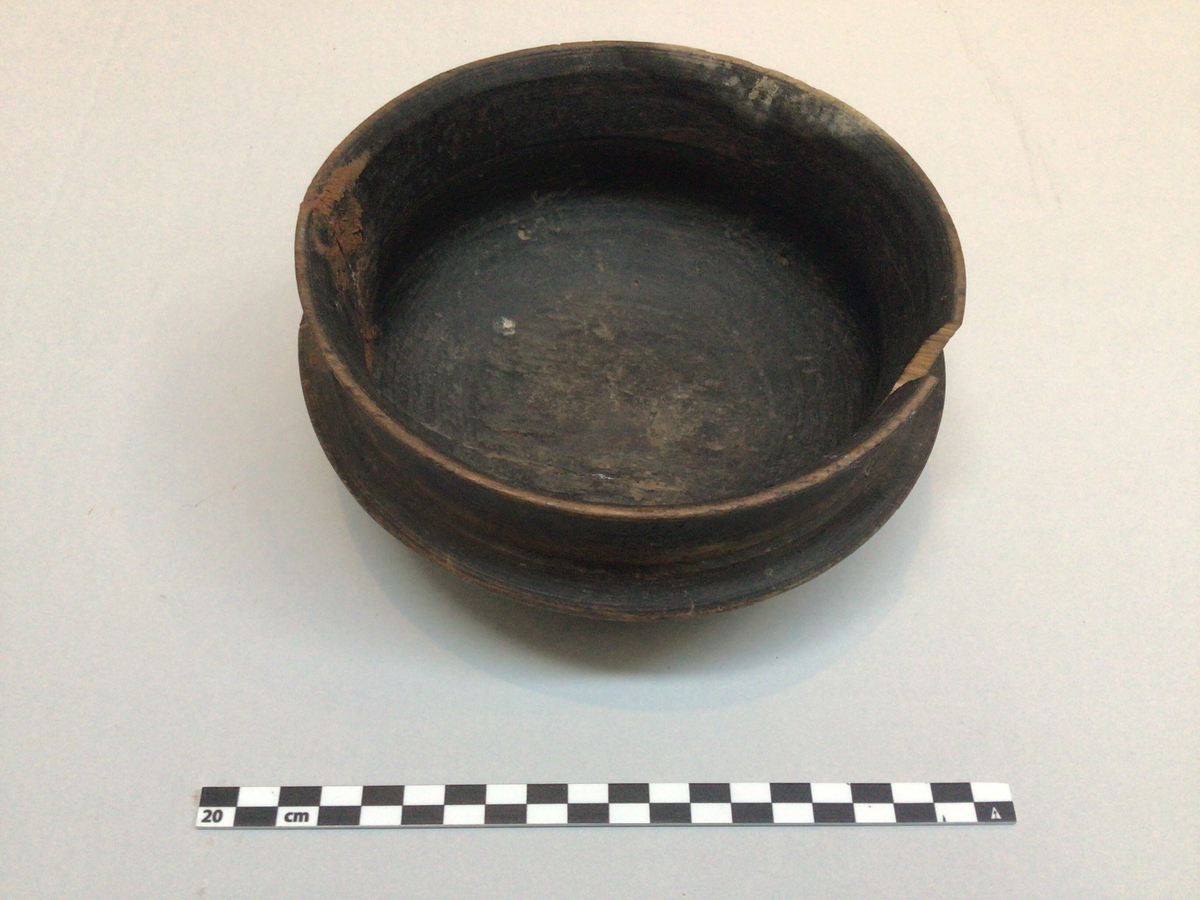 Dreid skål i tre, malt mørkbrun. Truleg brukt som ølbolle. Skåla har fotring, utvida og korpus mot skulder og munningsrand. Det er slått av eit stykke øvst i munning og denne biten ligg i skåla.. Skåla har ein tydeleg sprekk i botn som går mest heile vegen rundt og opp på sidene til munningsrand.