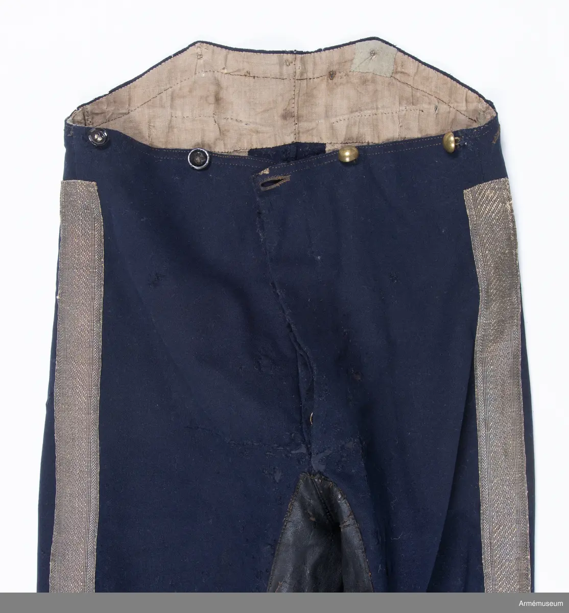 Mörkblå långbyxor med skinnskoning i baken och på benens insida, samt revärer av metallgalon i sidorna.

Byxorna är sydda av mörkblått kläde och har 4 cm breda revärer av silvergalon på benens utsidor. De är ursprungligen av en äldre modell med hel lucka fram, men har sytts om till gylf mitt fram, troligen i samband med att gylf fastställdes för långbyxor 1845. I varje sida syns spår efter luckan i form av ett smalt insnitt, samt ett igensytt knapphål.
Gylfen har dold knäppning med 4 enkla svartlackade knappar.
Byxorna är skinnskodda med brunt skinn i baken och på benens insidor, men det syns även rester efter en rad stygn ovanför knät på båda ben som eventuellt kan vara spår efter en äldre skinnskoning.
Byxorna är ofodrade, men har en infodring av oblekt bomullstyg i linningen upptill och en bit ner på framstycket. Infodringen är lappad på flera ställen.
På vänster byxben vid knät syns en stor lagad reva i tyget. Nertill vid fållen sitter i vänster byxben en sekundär hälla av svart resårband, samt en sekundär svart plastknapp. Dessa har troligen satts dit i samband med att byxorna varit utställda.
På insidan av höger bens fåll sitter två små knappar för fastsättning av hälla. En lapp eller lagning är dessutom iskarvad vid höger knä.
Byxorna har 3 knappar bak och 4 fram för fastsättning av hängslen. De två knapparna på höger sida fram är kullriga mässingsknappar, medan övriga är 4-hålsknappar av svartlackad metall.