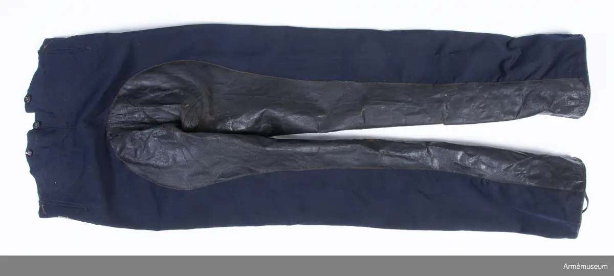 Mörkblå långbyxor med skinnskoning i baken och på benens insida, samt revärer av metallgalon i sidorna.

Byxorna är sydda av mörkblått kläde och har 4 cm breda revärer av silvergalon på benens utsidor. De är ursprungligen av en äldre modell med hel lucka fram, men har sytts om till gylf mitt fram, troligen i samband med att gylf fastställdes för långbyxor 1845. I varje sida syns spår efter luckan i form av ett smalt insnitt, samt ett igensytt knapphål.
Gylfen har dold knäppning med 4 enkla svartlackade knappar.
Byxorna är skinnskodda med brunt skinn i baken och på benens insidor, men det syns även rester efter en rad stygn ovanför knät på båda ben som eventuellt kan vara spår efter en äldre skinnskoning.
Byxorna är ofodrade, men har en infodring av oblekt bomullstyg i linningen upptill och en bit ner på framstycket. Infodringen är lappad på flera ställen.
På vänster byxben vid knät syns en stor lagad reva i tyget. Nertill vid fållen sitter i vänster byxben en sekundär hälla av svart resårband, samt en sekundär svart plastknapp. Dessa har troligen satts dit i samband med att byxorna varit utställda.
På insidan av höger bens fåll sitter två små knappar för fastsättning av hälla. En lapp eller lagning är dessutom iskarvad vid höger knä.
Byxorna har 3 knappar bak och 4 fram för fastsättning av hängslen. De två knapparna på höger sida fram är kullriga mässingsknappar, medan övriga är 4-hålsknappar av svartlackad metall.