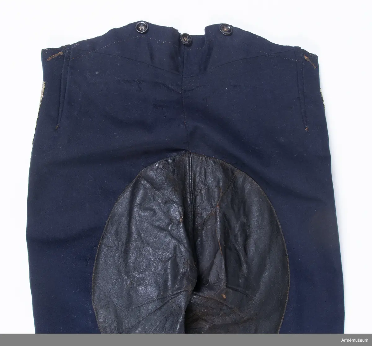 Mörkblå långbyxor med skinnskoning i baken och på benens insida, samt revärer av metallgalon i sidorna.

Byxorna är sydda av mörkblått kläde och har 4 cm breda revärer av silvergalon på benens utsidor. De är ursprungligen av en äldre modell med hel lucka fram, men har sytts om till gylf mitt fram, troligen i samband med att gylf fastställdes för långbyxor 1845. I varje sida syns spår efter luckan i form av ett smalt insnitt, samt ett igensytt knapphål.
Gylfen har dold knäppning med 4 enkla svartlackade knappar.
Byxorna är skinnskodda med brunt skinn i baken och på benens insidor, men det syns även rester efter en rad stygn ovanför knät på båda ben som eventuellt kan vara spår efter en äldre skinnskoning.
Byxorna är ofodrade, men har en infodring av oblekt bomullstyg i linningen upptill och en bit ner på framstycket. Infodringen är lappad på flera ställen.
På vänster byxben vid knät syns en stor lagad reva i tyget. Nertill vid fållen sitter i vänster byxben en sekundär hälla av svart resårband, samt en sekundär svart plastknapp. Dessa har troligen satts dit i samband med att byxorna varit utställda.
På insidan av höger bens fåll sitter två små knappar för fastsättning av hälla. En lapp eller lagning är dessutom iskarvad vid höger knä.
Byxorna har 3 knappar bak och 4 fram för fastsättning av hängslen. De två knapparna på höger sida fram är kullriga mässingsknappar, medan övriga är 4-hålsknappar av svartlackad metall.