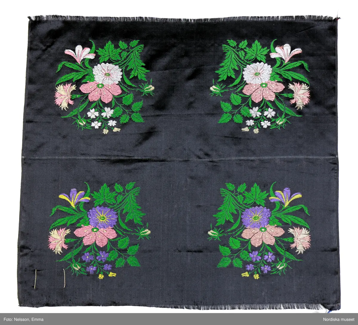 På svart botten två par speglade buketter avpassade för bindmössor. Gröna blad, blommor i vitt, rosa och beige i ena paret, i andra paret blommor i violett, gult, rosa och beige. Mellan mössstyckena en vit rand. I stadkanten, längst upp och längst ner, spår av röda trådmarkeringar (för att markera antal stycken vid vävningen?)
 I ena hörnet finns en  pappersetikett fäst med lintråd där den ena knuten har spår efter ett lacksigill. Tryckt bild i ljusblått/vitt med texten: "Svensk tillverknings Stämpel År 1852 No. 713" samt med handskrift C G(?) Mårtenson. I ett annat hörn finns på baksidan en tydlig  hallstämpel i rött med texten:" Svensk tillv.st.  Stockholm.
I museets samling bindmössor finns flera av denna typ se t.ex. 990258a från Ångermanland samt 3 st från Järna i Dalarna  93311, 93 635 och 60748. Märkligare är att sådana avpassade mösstycken även har använts till folkliga livstycken. Se t.ex från Alfta sn i Hälsingland  inv .nr 3192 och 190428. 
Se även avpassat mössbroderi i tambursöm på siden inv. 19607 och 19608.
/Berit Eldvik 2011-01-26
Analys gjord av Martin Ciszuk 2011-01-25:
 Material och teknik: Broscherad satin
1 varp:
Silke, organzin svart
Varp-stygn: 6? trådar
Varptäthet: ca 132 trådar/cm

2 inslag: förhållande: 2:1 a.a.b
a: botteninslag: silke, tram utan synlig snodd, svart (+ vitt i ränder mellan mössstyckena)
b: broscherat mönsterinslag: silke, tram, utan synlig snodd, tjockare än botteninslag, grönt vitt, rosa, beige, violett, gult.

Inslags-stygn: 1 passé = 2 botteninslag+ 3 broscherade inslag
Inslagstäthet: 18 passéer = 36 botteninslag/ cm
Stadkant: 0,3 cm, panama + tuskaft
Botten: Satin 7.1 stigningstal 5, broscherade inslag flotterar på avigsidan      

Mönster:1 broscherat inslag flotterar över satin, bundet par decoupure, andra broscherade inslag flotterar på avigsidan
Tillverkningssätt:
 Vävd med rätsidan ner i vävstol med 8 bottenskaft och jacquardmaskin med ca 350 krokar 2 spegelvända rapporter, och kortkedja med ca 800 kort 
 Kommentar:
Mössa med samma mönster med blå botten med vita, rosa och gula blommor finns i Nordströms samling, Norrtälje
Mösstyg förekommer i Kommerskollegiums fabriksberättelser 1765-1848 därefter sporadiskt fram till 1861. De värderas till 1 daler silvermynt/stycke 1766, till 4/5 riksdaler 1780,  till ¾  daler banco1790-1813, till 1 riksdaler banco 1814-58 och till 1½ daler riksmynt 1861. Förändringarna i värde bör främst tolkas som justeringar mot inflation och valutaförändringar. 1829 visar en felskrivning i fabriksberättelsen att 1 stycke var ½ aln (29 alnar har ändrats till 58 stycken)
1852 vävde endast Casparsson & Schmidt mösstyg. NM 92 745 bör vara tillverkad där, trots namnet Mårtenson på etiketten.

Endast några fabriker rapporterade att de vävde mösstyg varje år (fler vid 1800-talets början och 1700-talets slut), det var inte alltid de största fabrikerna:
Casparsson & Schmidt 1809, 1838- 61
GW Fagerlin 1835-38, 1841
P Berger Ersson(Carlsson?) & Co. -1836 hade den sammanlagt största produktionen under 1800-talet
Mazér 1817-20, 1828, 1833
A. Norman & Co. 1832
Z. Fagerlund & Co 1801-07, 1829
MG Begström 1826
S. Glassl 1818-24
G. Hellsingius 1814-15
Lindström Magnus -1804, 1807-08
Schönherr C.J. & Co. -1808
Fritziska fabriken 1803-07
Arnberg F.M. 1804
Mellring Carl & Sven 1800, 1802, 1804
Von der Osten & Co. 1803
Gisiko A.S. -1802
Åhman Abraham 1801
Billmarks Sterbhus -1800
Enström Samuel -1800