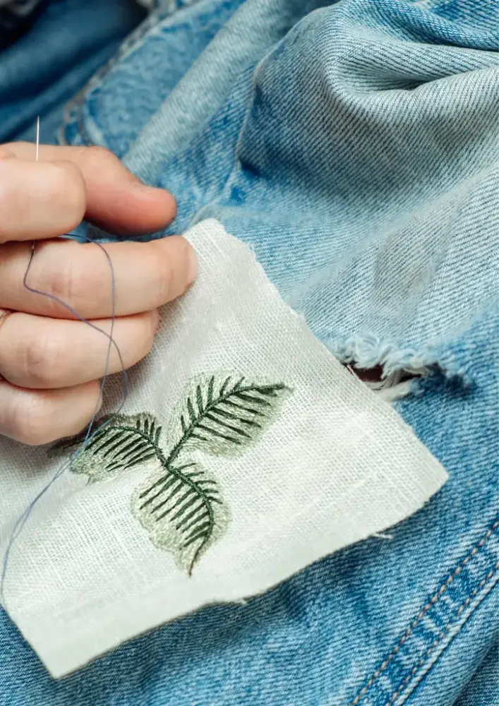 Håndsydd grønne blader sys over hullete dongeri