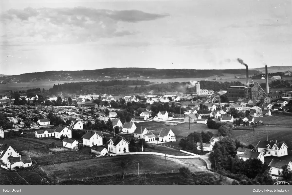 Boliger og fabrikkanlegg på Greåker i Tune ca. 1930 med fabrikken og jernbanestasjonen, sett fra  Greåker fort. Postkort.