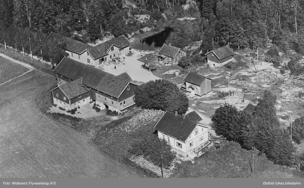 Flyfoto  av Bergby gård (Fossengen) i Varteig 1959, bakerst til venstre er smie og verksted, kjeller, bryggerhus, bu, våningshus, og vedskjul, fjøs og stall og låve foran til venstre.
Bilde nummer to er utsnitt fra tunet med bilde av lastebil.