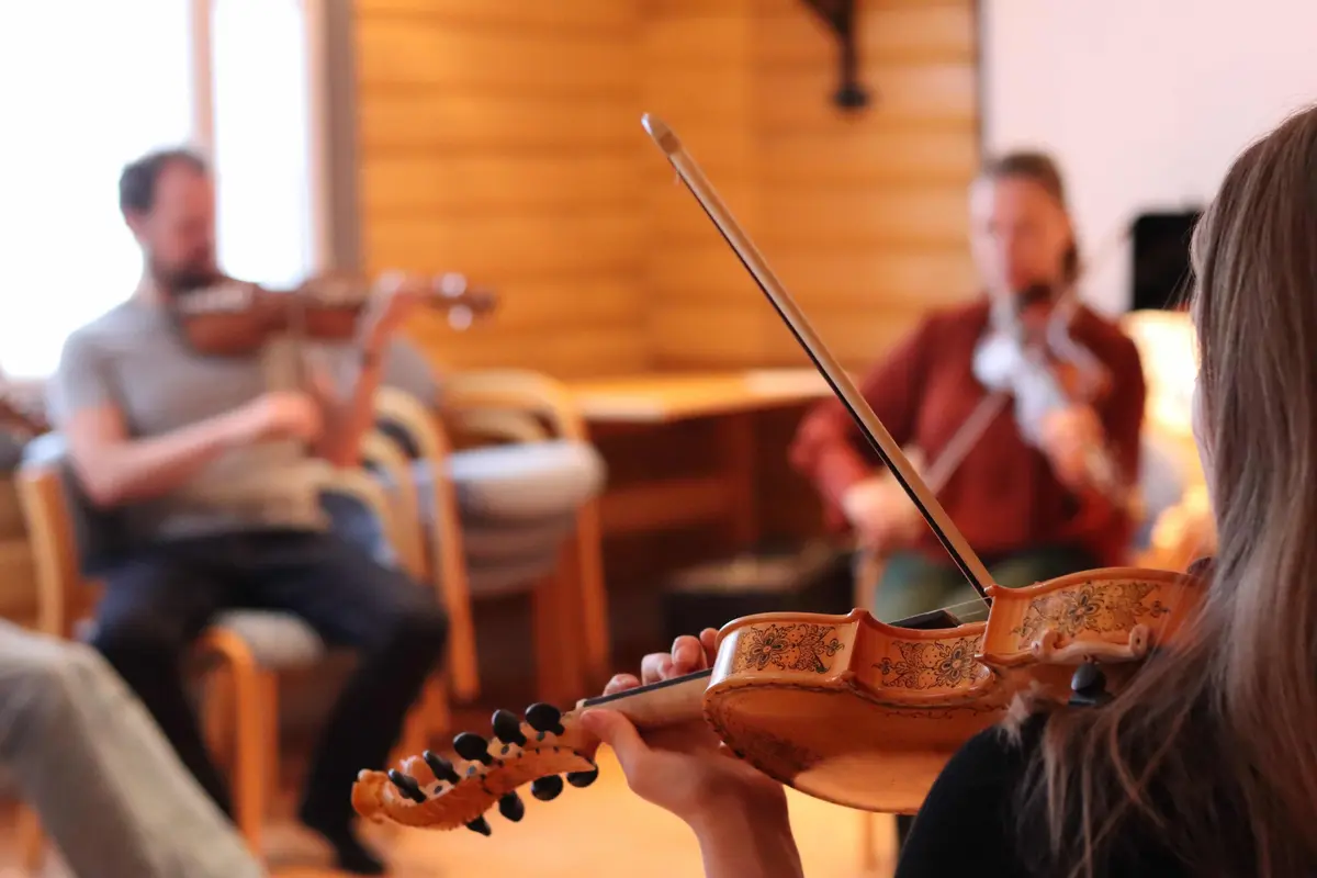 Bilde av en fele i forgrunnen med to uklare felespillere i bakgrunnen. 