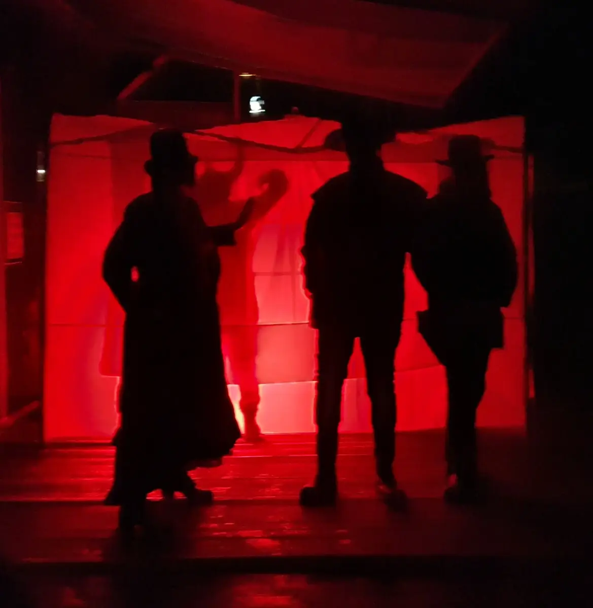 Sorte silhuetter i rødt lys, to westernmenn og en kvinne med kjole og flotthatt