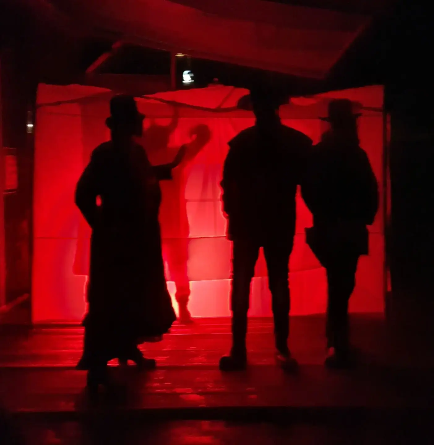 Sorte silhuetter i rødt lys, to westernmenn og en kvinne med kjole og flotthatt